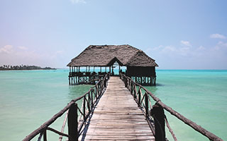 a pier stretching out over clear water to a hut